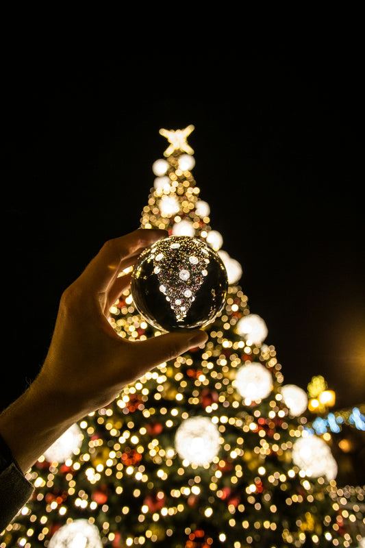 person lifting bauble near Christmas tree