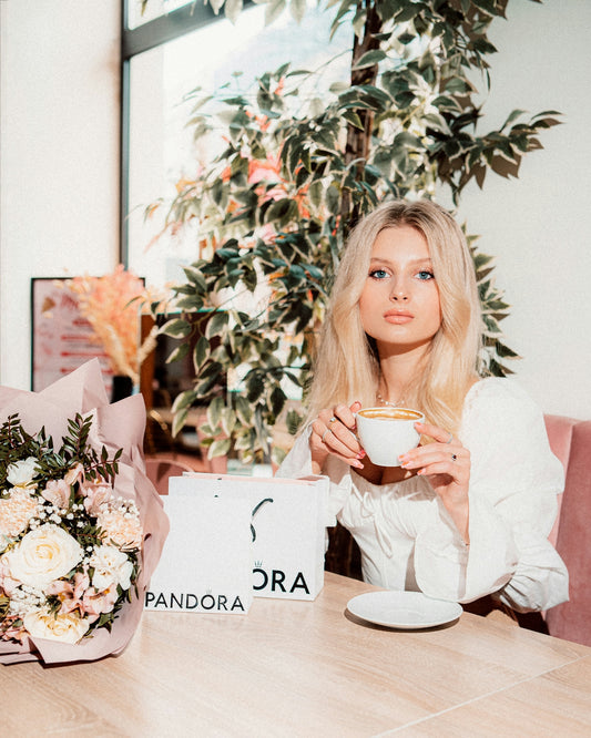Young woman sips tea with pandora bags and flowers.