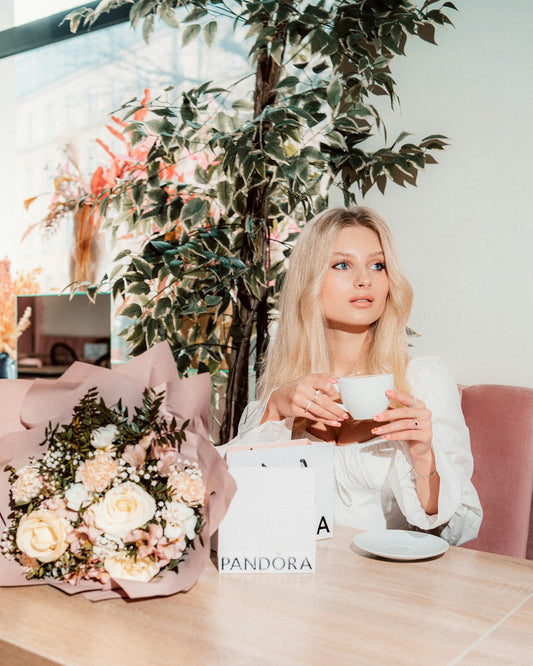 Blonde woman with coffee, flowers, and a pandora bag.